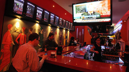 Taste of Dahntahn on Liberty Avenue features a large square bar, surrounded by high-backed red-and-white leather stools. The dining room (behind the bar) is narrow with booths along one side and tables and chairs on the other.