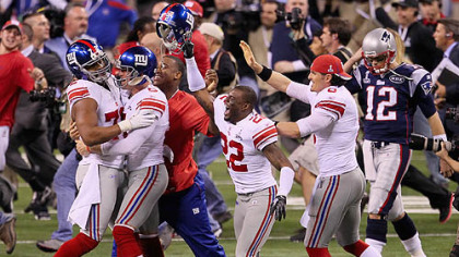 New York Giants players celebrate in front of Tom Brady of the New England Patriots after defeating the New England Patriots by a score of 21-17 during Super Bowl XLVI at Lucas Oil Stadium.