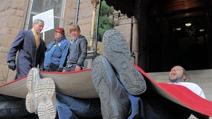 Raheem Crawford, right, 28, of the North Side and other members of One Pittsburgh lie under a red carpet urging patrons to step on them at the Duquesne Club, Downtown, on Friday.  Gov. Tom Corbett attended a luncheon with his supporters at the club. The group chanted that Mr. Corbett's budget steps on "the 99 percent."