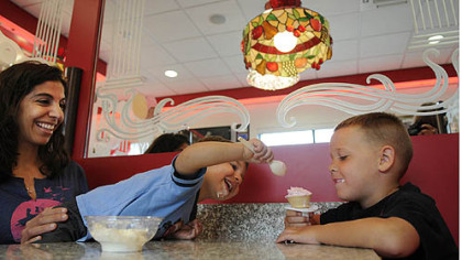 Brea Robinson watches as her son, Elijah, 2, grabs ice cream from his friend, Dominic Thomas, 6, Friday morning at the grand re-opening of the ice cream parlor at Sarris Candies in Canonsburg.
