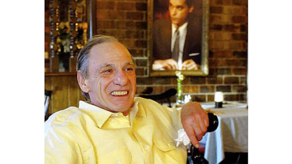In this Feb. 22, 2005, photo, Henry Hill sits in the dining room of the Firefly restaurant in North Platte, Neb., with a portrait of actor Ray Liotta portraying Mr. Hill in the movie "GoodFellas" hanging on the wall behind him.