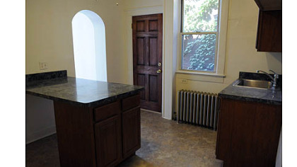 The first-floor kitchen has hardwood cabinets with a maple stain, laminate counter tops and vinyl-tile floor. Arched openings lead to a bathroom and the breakfast nook.