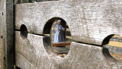 Tour guide Kaitlin Davis is seen through a hole in the pillory at Historic Hanna's Town.