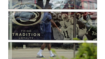 A student is reflected in the window of the Mildred and Louis Lasch Football Building on Penn State's main campus in State College.