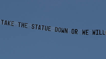 A plane flying over the Penn State University campus in State College, pulls a banner reading "Take the statue down or we will" today.