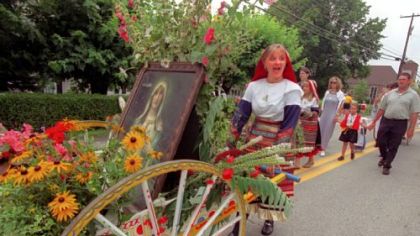 In 2000: Ashley Kessler responds to spectator cheering as she pushes a cart filled with flowers and a portrait of Our Lady of Mount Carmel as she and other parishioners march in the parade after Mass at St. Bartholomew Catholic Church, Crabtree, down the street and back.