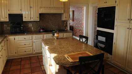 The updated kitchen features a cream-colored coffered ceiling and cabinetry, and red Mexican ceramic tile floors. A center island topped with Venetian Gold granite seats three.