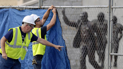 Workers place a tarp on a fence in front of the statue of former Penn State football coach Joe Paterno before removing it.