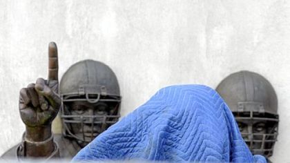 The Joe Paterno statue, its head covered in a tarpaulin but its upraised finger still visible, is prepared for removal Sunday from the monument outside Beaver Stadium.