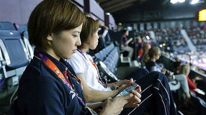 Japan's Miyuki Maeda checks at her iPhone as she watches badminton matches in progress at the Summer Olympics, Tuesday, July 31, 2012, in London. The 2012 games are being shaped, shaken and indisputably changed by the social media revolution.