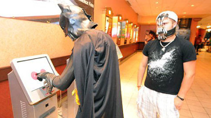Dustin Briggs, dressed as Batman, buys a ticket to the midnight showing of "The Dark Knight Rises" at AMC Loews Waterfront, while Tanner Kefover, dressed as Bane, looks on.