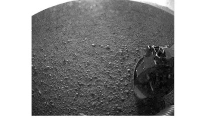 One of the first images taken by NASA's Curiosity rover, which landed this morning on Mars. The image was taken through a "fisheye" wide-angle lens. The clear dust cover that protected the camera during landing has been sprung open. Part of the spring that released the dust cover can be seen at the bottom right, near the rover's wheel.