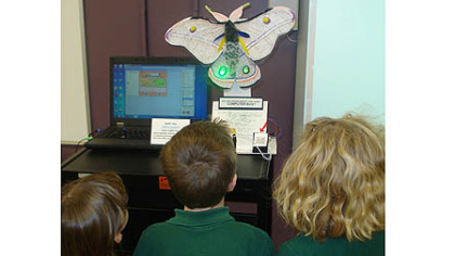 A group of children look at the moth robot and the computer where the program runs.