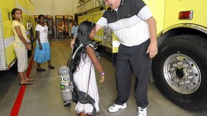Regina Anand, 8, from Marshall, tries on an oxygen tank with fireman John Ashbaugh during a tour of the station.  Regina donated the money she received at her first communion party to the Marshall Township Volunteer Fire Department.